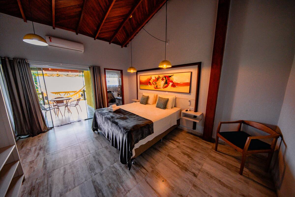 A bedroom with a large bed, a wooden chair, a desk, and a painting on the wall.