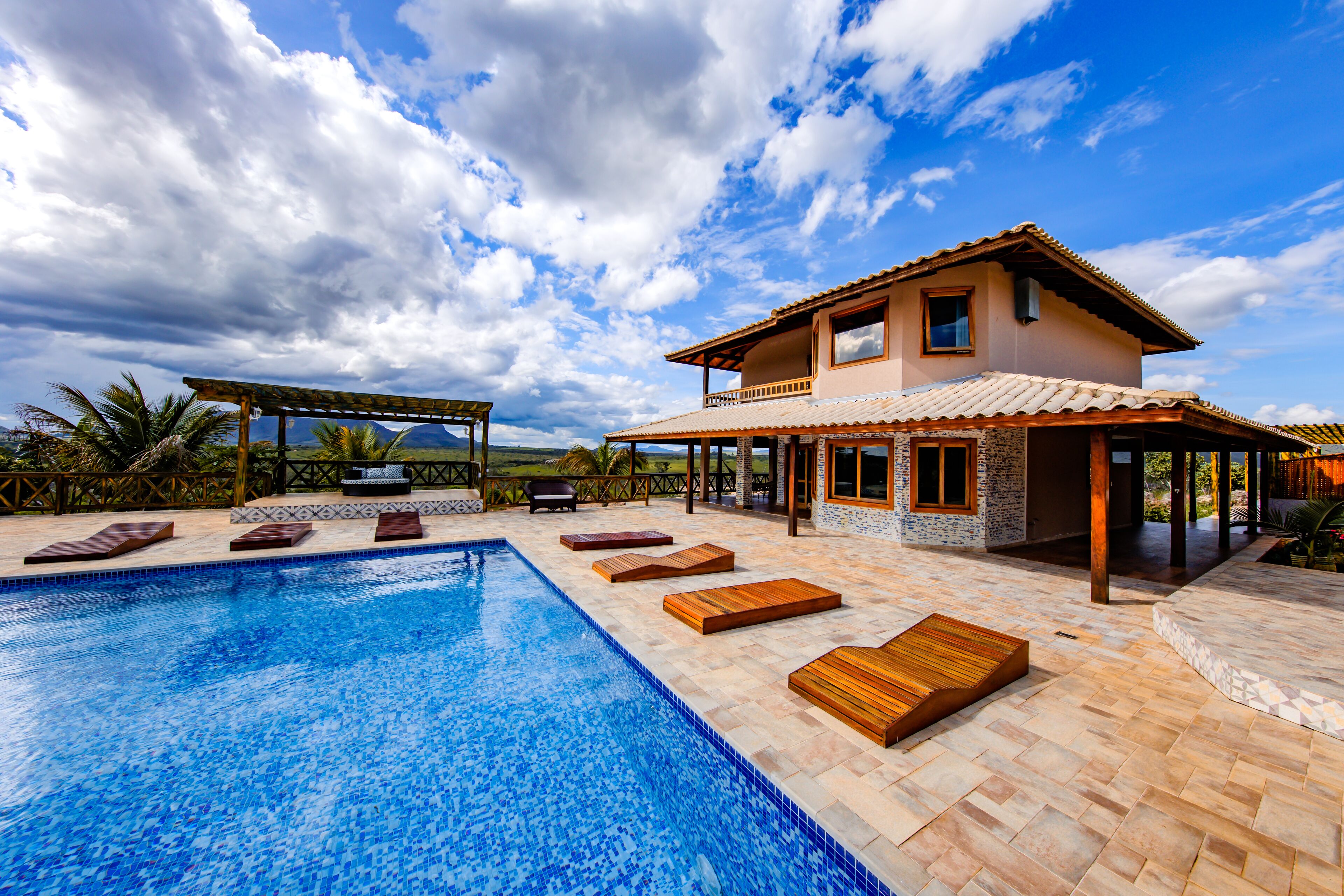A poolside area with a swimming pool, wooden loungers, and a covered seating area.