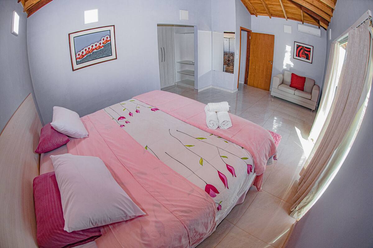 A bedroom with a bed, pillows, a wardrobe, a sofa, and a window with curtains.