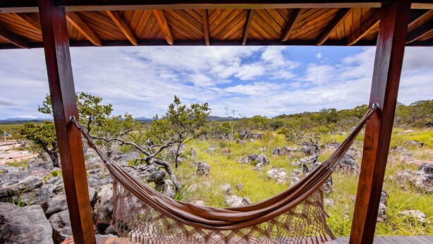 Una hamaca bajo una pérgola de madera con vista a un paisaje rocoso y vegetación escasa.