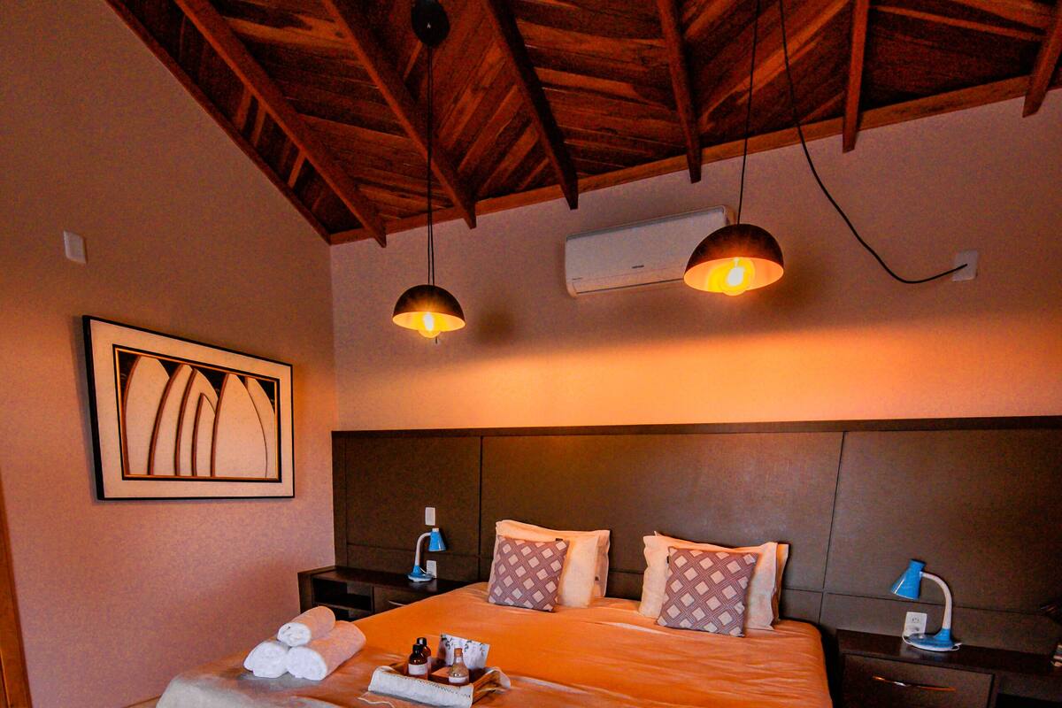A hotel room with a large bed, two bedside tables, a wooden ceiling, and a framed artwork on the wall.