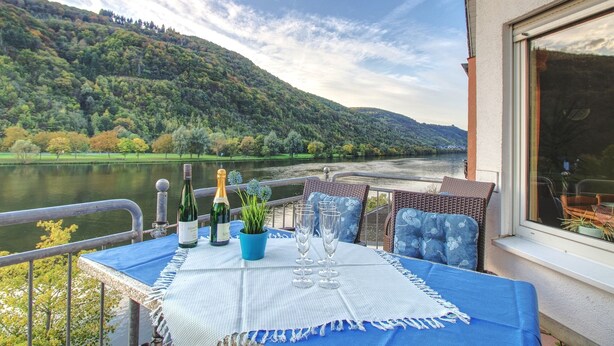 A terrace with a table set for two, overlooking a river and hills.