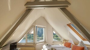 A bedroom with a sloped ceiling, a bed with pillows, a TV, and a radiator.