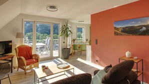 A spacious living room with a large window, a dining area, and a view of a lake.