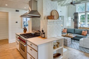 Enjoy cooking in the kitchen with a stainless steel stove, range hood, and oven, then relax in the adjacent living area with a sofa and coffee table.