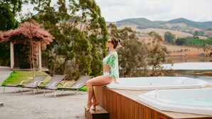 Una mujer sentada en una terraza de madera con jacuzzis, rodeada de sillones de descanso y un pabellón.