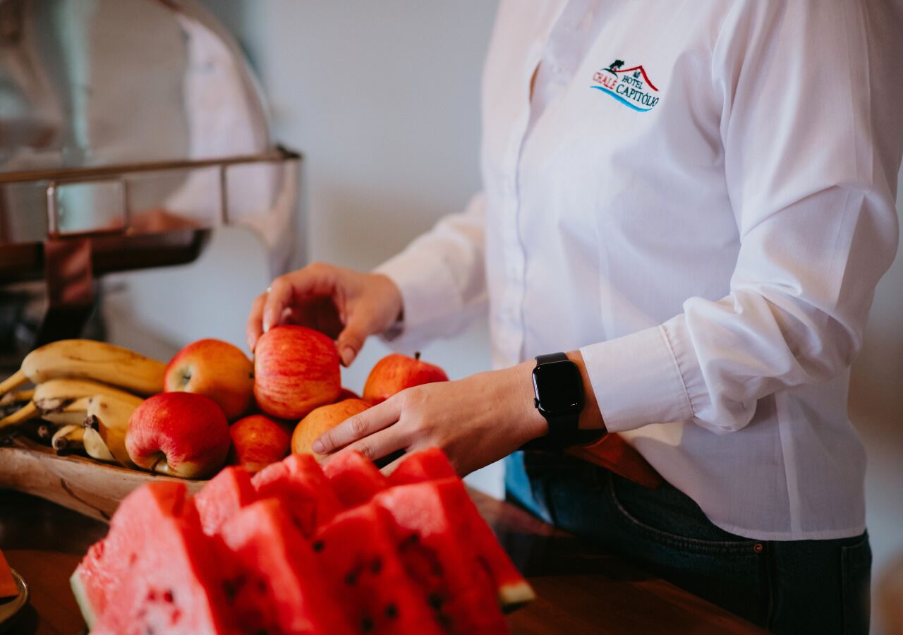 A person in a white shirt with a logo, handling fruits including apples and a watermelon.