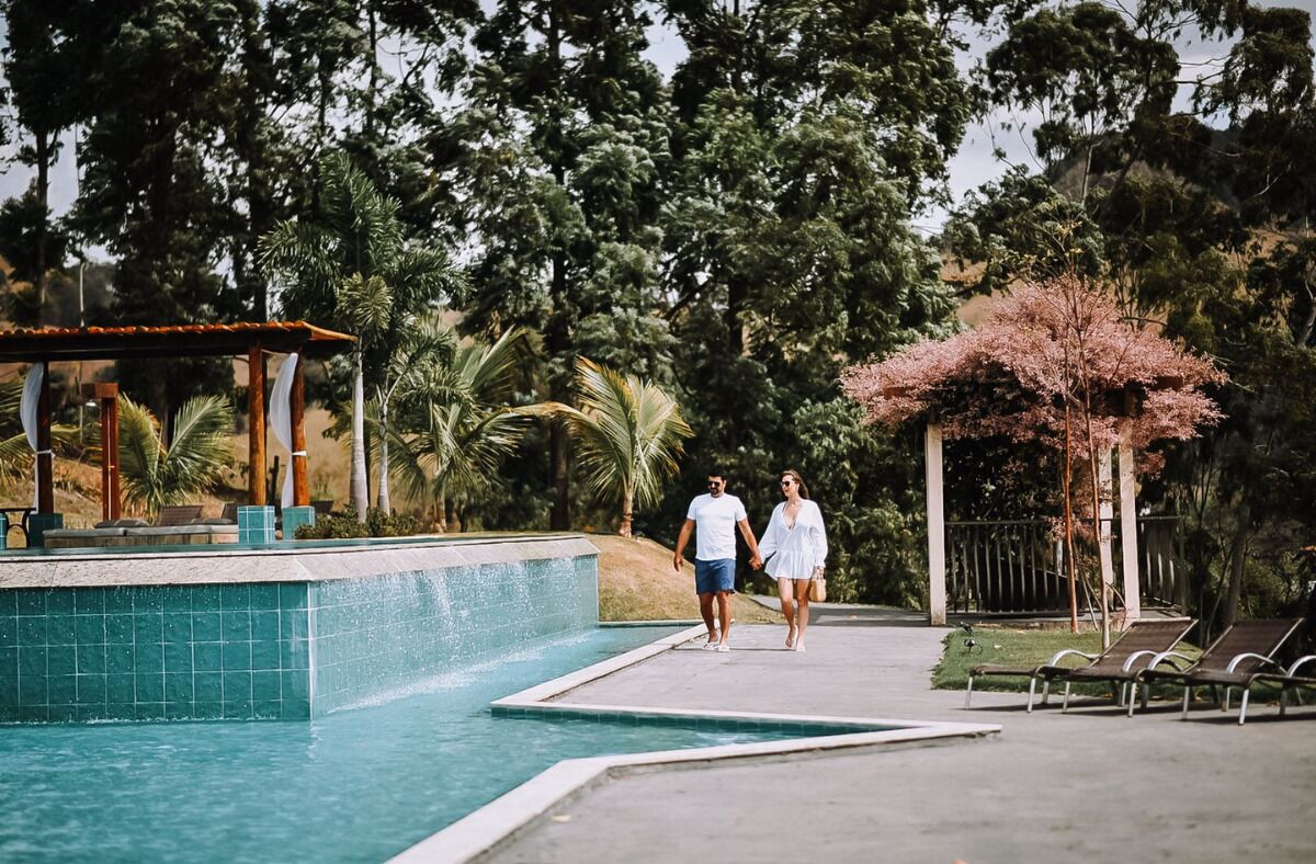 A couple walking by a pool with a gazebo and palm trees in the background.
