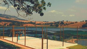 Una playa con una zona arenosa, una estructura de madera y vistas a un lago y colinas al fondo.