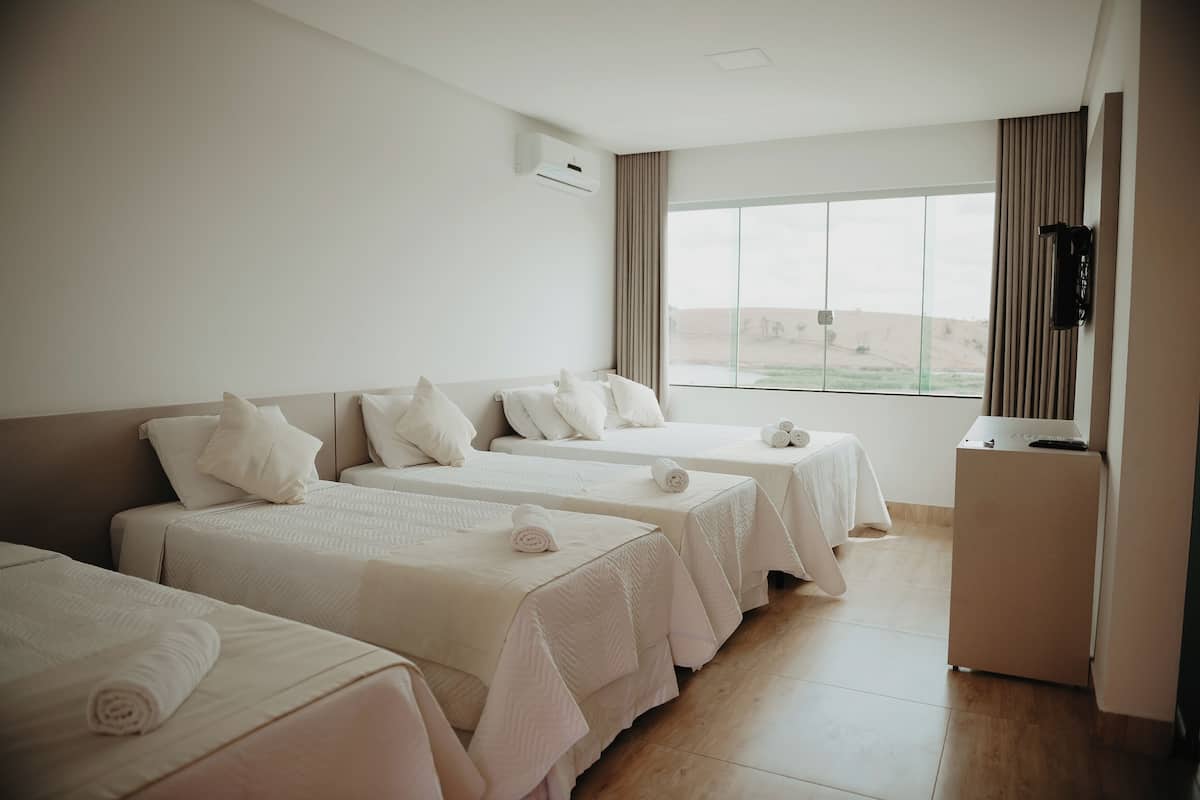 Habitación de hotel con tres camas, un escritorio pequeño y una ventana con vista al desierto.