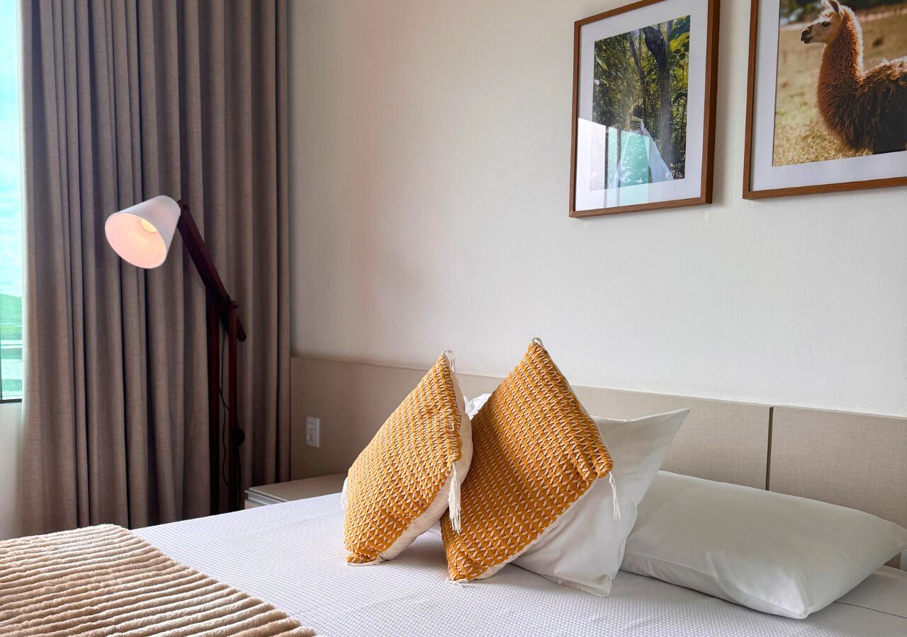 A neatly made bed with white and yellow pillows, a bedside lamp, and framed pictures on the wall.