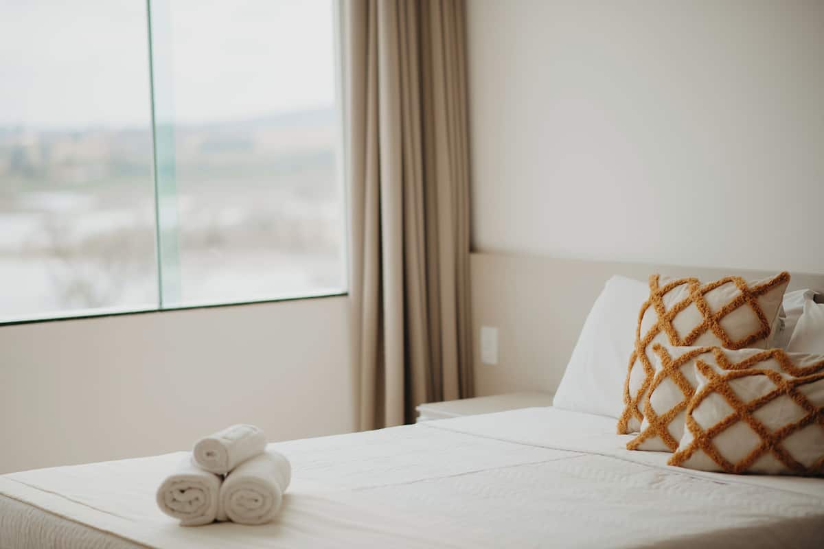 Habitación de hotel con cama, ventana con cortinas y toallas dobladas sobre la cama.