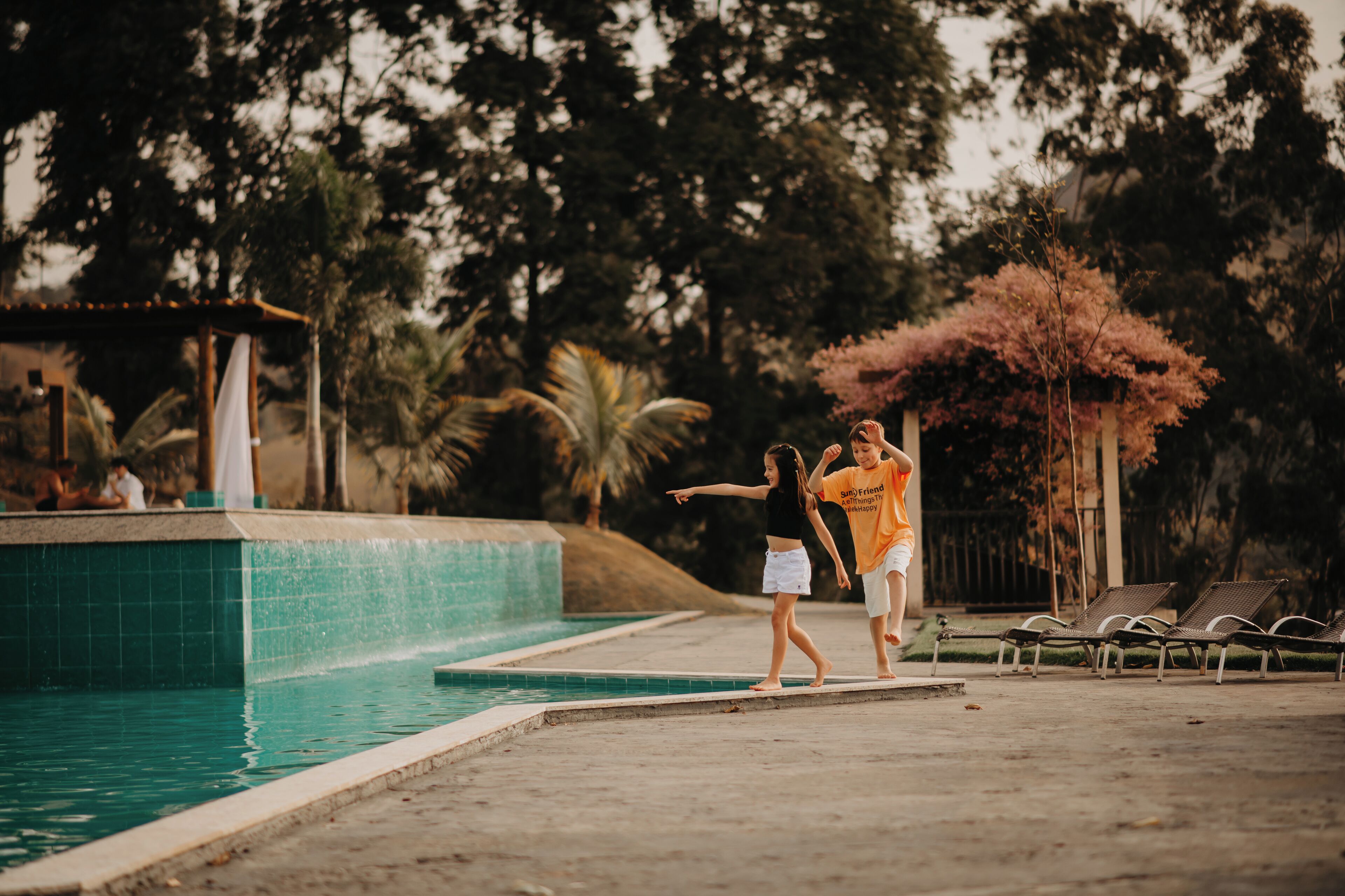 A swimming pool with a tiled edge and a few lounge chairs in the background.