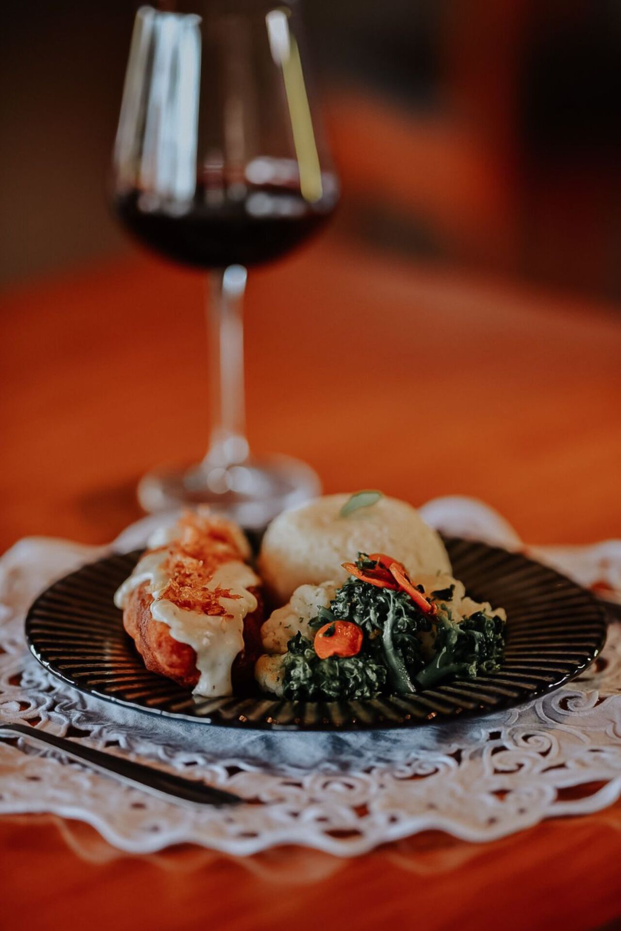 A plate of food with a glass of red wine on a table with a lace tablecloth.