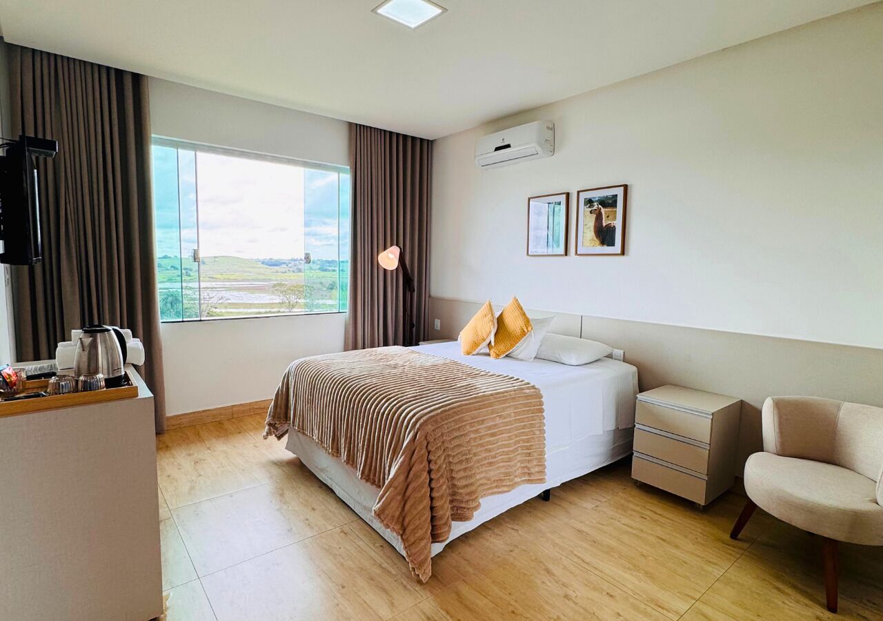 Habitación de hotel con cama, mesita de noche, silla y vistas al exterior.