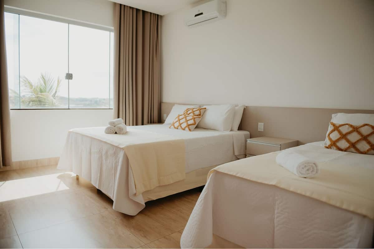 Habitación de hotel con dos camas, un ventanal grande y vistas a palmeras.