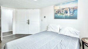 A bedroom with a bed, a painting of a cityscape, and a white door.