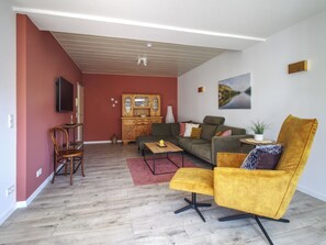 A living room with a sofa, armchair, wooden cabinet, and a television.