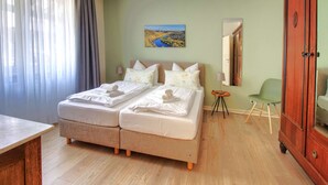 Une chambre d’hôtel avec deux lits, une armoire en bois, une chaise verte et un tableau au mur.