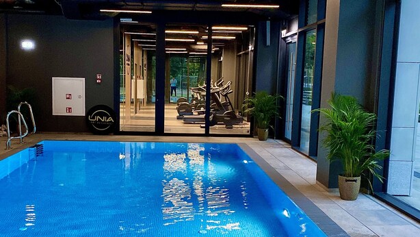 An indoor swimming pool with clear water, surrounded by walls and a ceiling with linear lighting fixtures. - Easy Rent Apartments - CRYSTAL (Lublin)