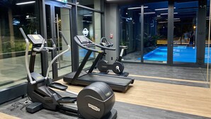 A gym with treadmills, an elliptical, and a stationary bike, with a pool visible through the glass doors. - Easy Rent Apartments - CRYSTAL (Lublin)