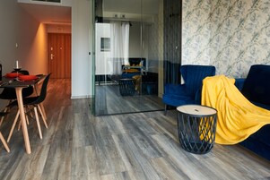 A modern living room with a glass partition, a dining area with a table and chairs, and a sofa with a yellow blanket.