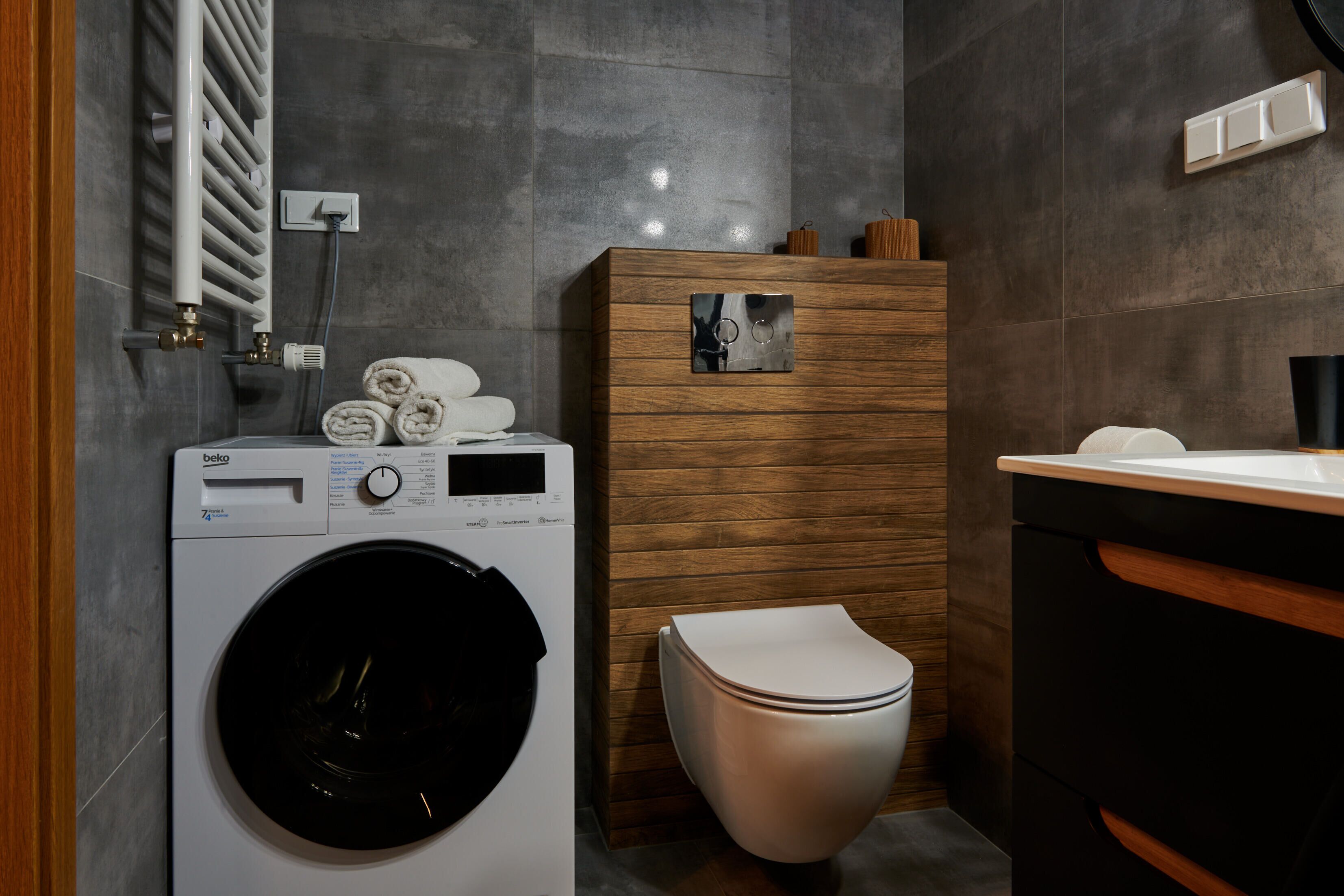 A modern bathroom with a built-in washing machine, a toilet, and a wooden vanity with a mirror.