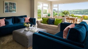 Una sala de estar con un sofá azul, un reposapiés estampado y vistas al exterior a través de ventanas amplias.