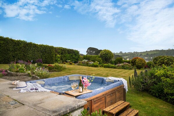 A hot tub with a wooden cabinet, a bottle of wine, and glasses on a tray.
