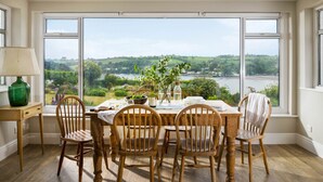 Comedor con una mesa dispuesta para cuatro, sillas de madera, una lámpara y vistas a un lago y vegetación.