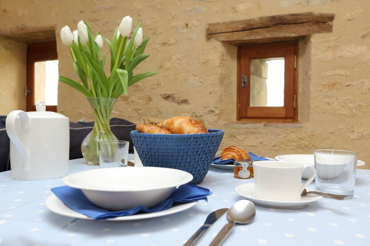 A breakfast table with croissants, a vase of tulips, and a pitcher of water.