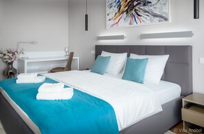 A modern hotel room with a large bed, a bedside table, a desk, and a chair.