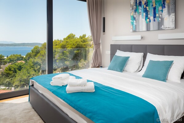 Une chambre à coucher moderne avec un grand lit, une vue sur la mer et un tableau accroché au mur.
