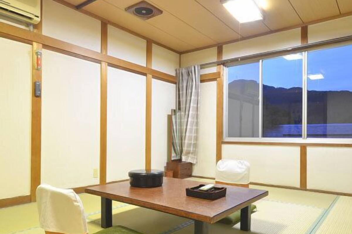 Una habitación con esteras de tatami, una mesa baja, cojines y vistas a las montañas.