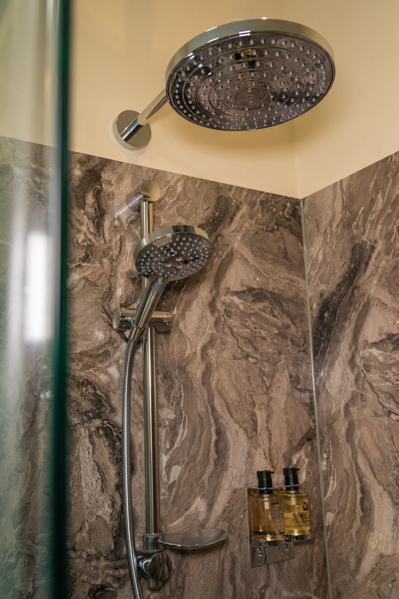 Un baño con ducha, cabezal de ducha de mano y dos botellas de artículos de aseo.