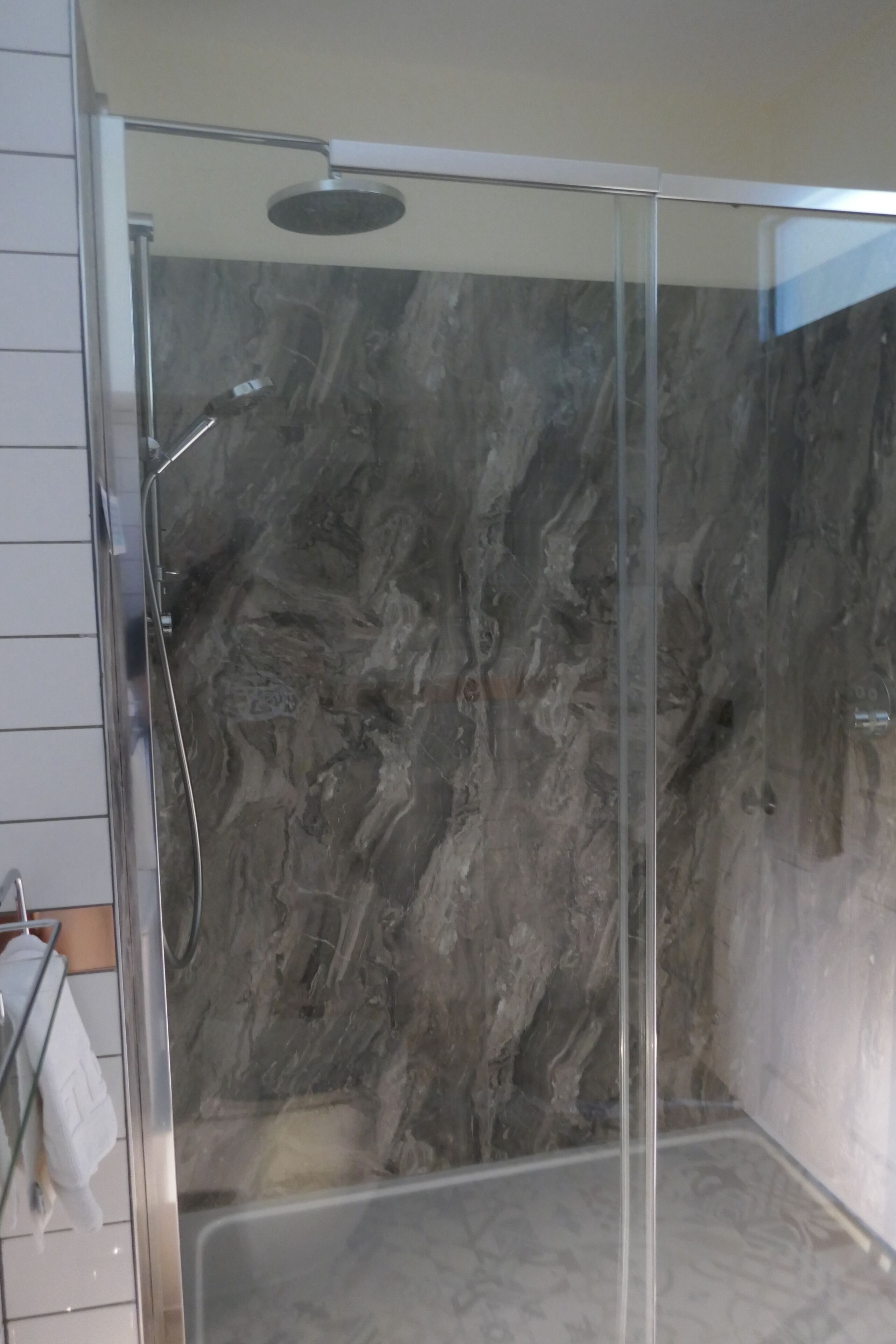 A glass-enclosed shower with a marble wall.