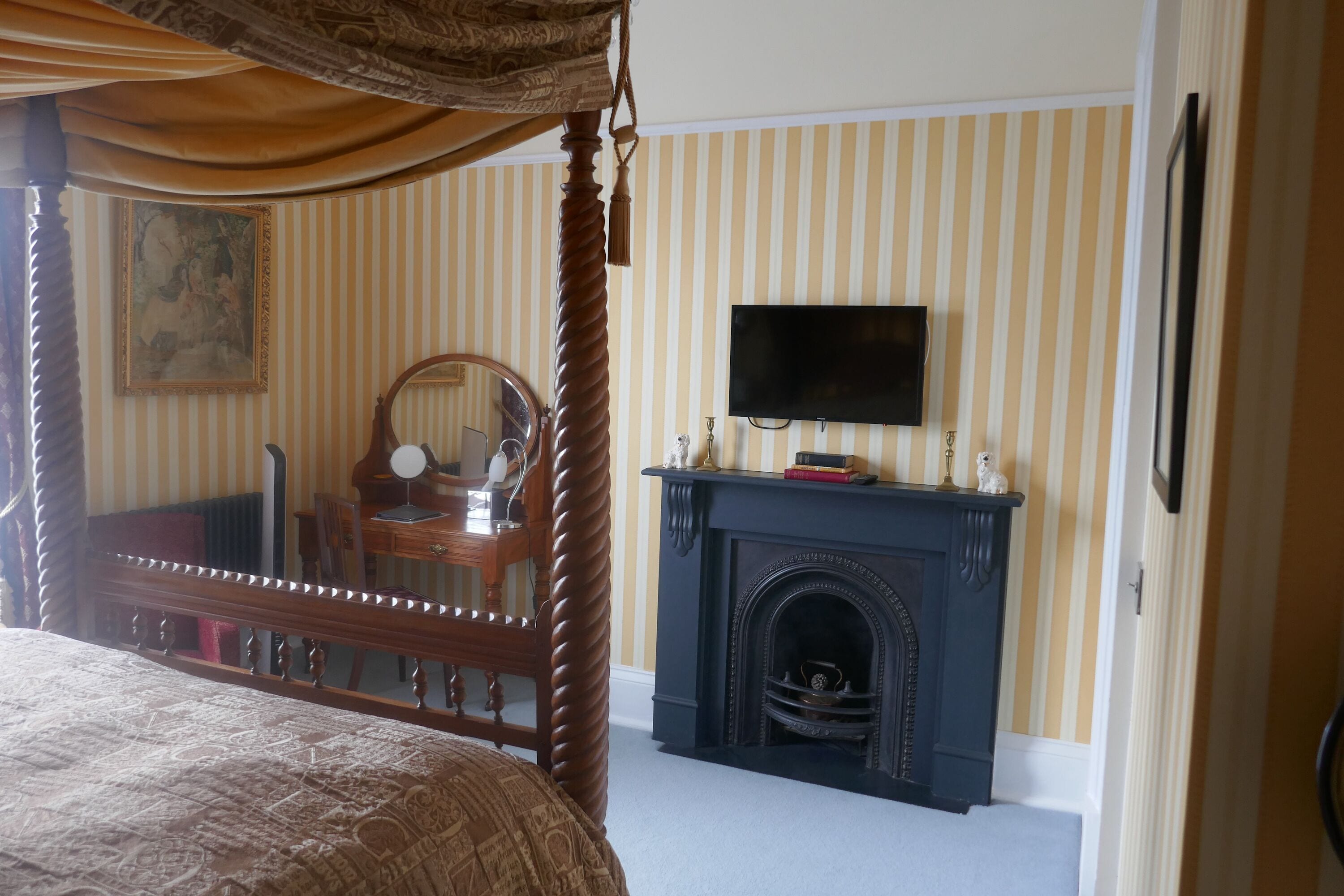 A bedroom with a four-poster bed, a fireplace, a television mounted above it, and a striped wallpaper design.