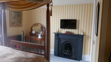 A bedroom with a four-poster bed, a fireplace, a television mounted above it, and a striped wallpaper design.