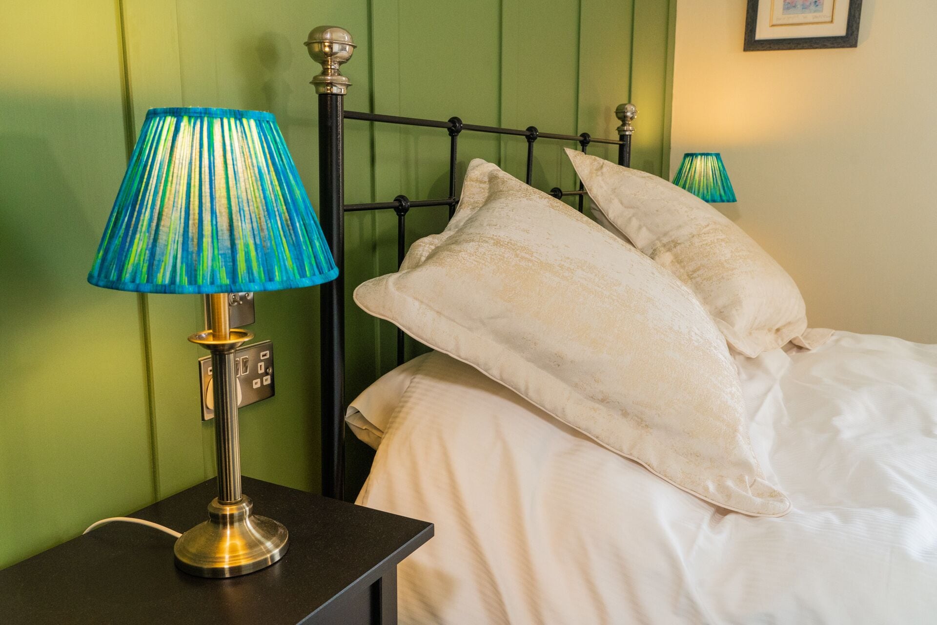 A bed with white linens and two pillows, a nightstand with a lamp, and a green wall.