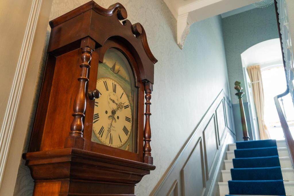 A wooden grandfather clock in a hallway with a blue carpeted staircase.