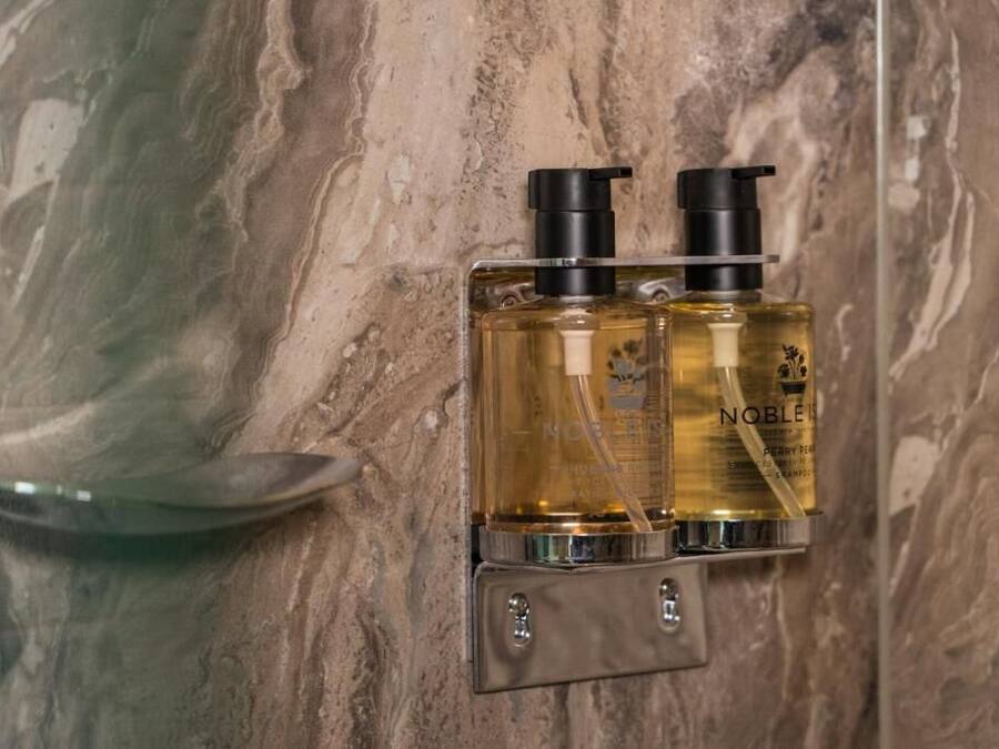 Two bottles of Noble body wash on a marble wall.