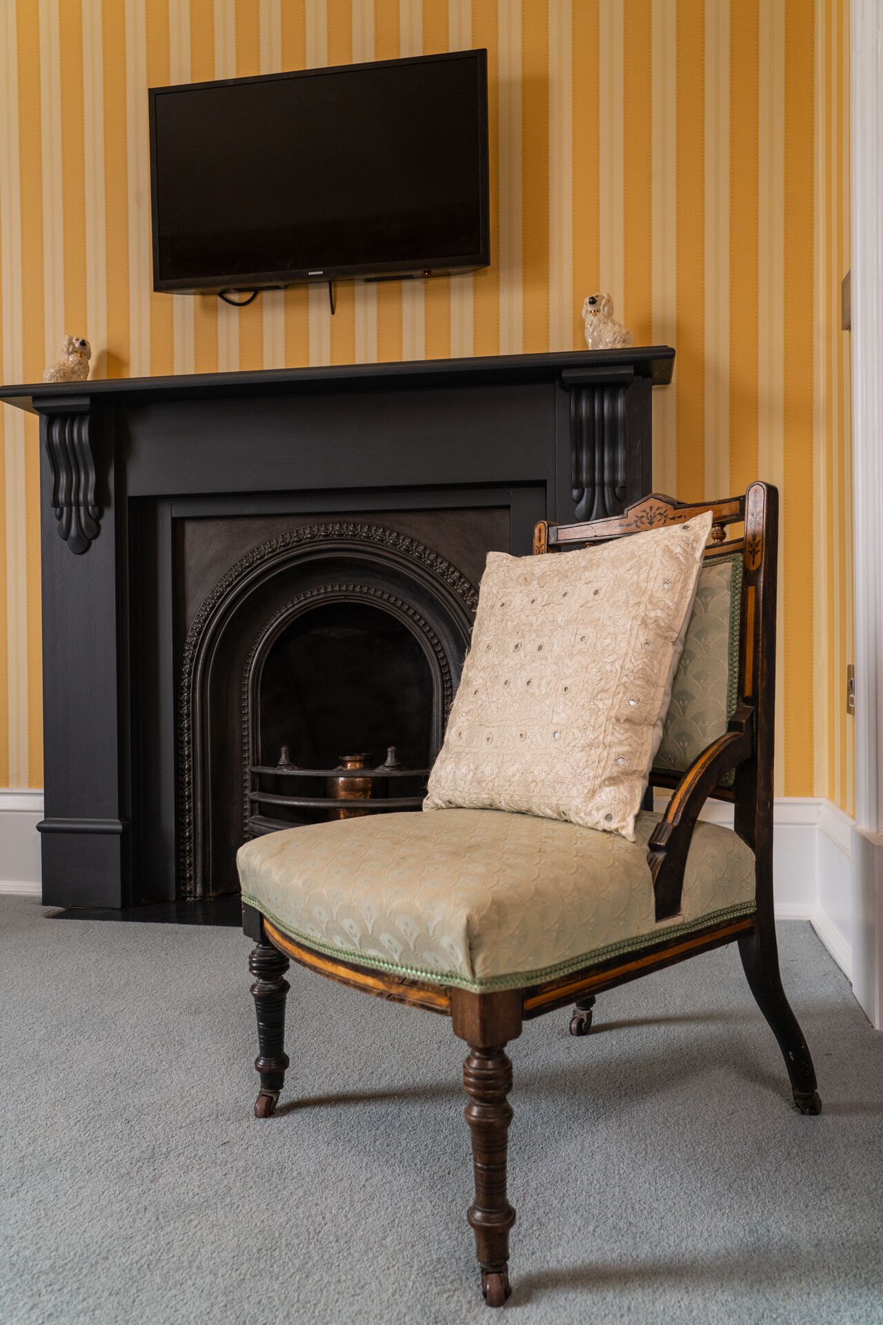 A chair with a cushion in front of a fireplace with a television mounted above it.