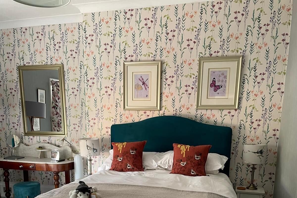 A neatly arranged bedroom with a bed, two bedside tables, a mirror, and floral wallpaper.