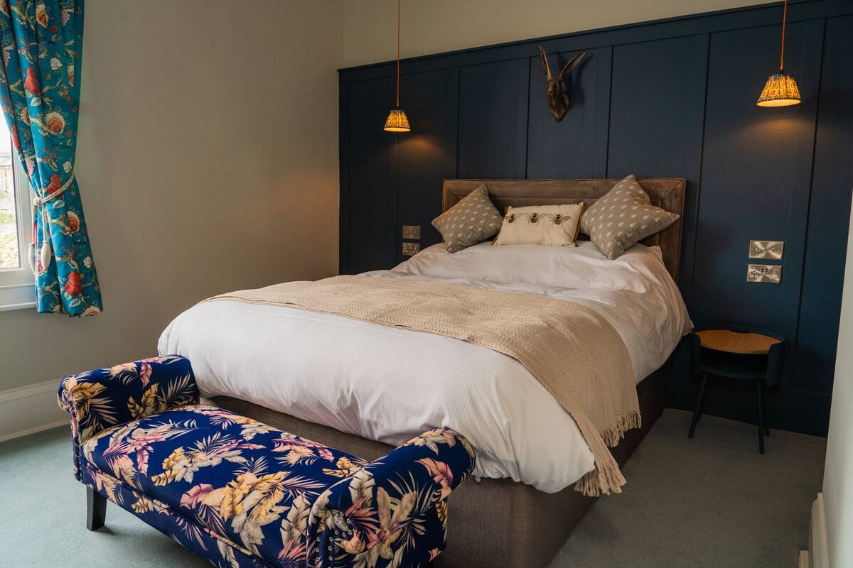 A bedroom with a bed, a nightstand, a chair, and a wall-mounted lamp.
