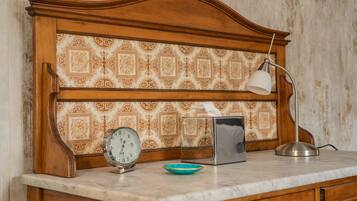 A wooden cabinet with a patterned wallpaper, a clock, a tissue box, a lamp, and a bowl on a marble countertop.