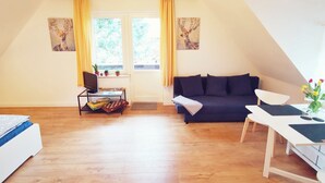 Une pièce chaleureuse avec un plafond en bois, un canapé bleu foncé, un bureau blanc et une fenêtre ornée de rideaux jaunes.