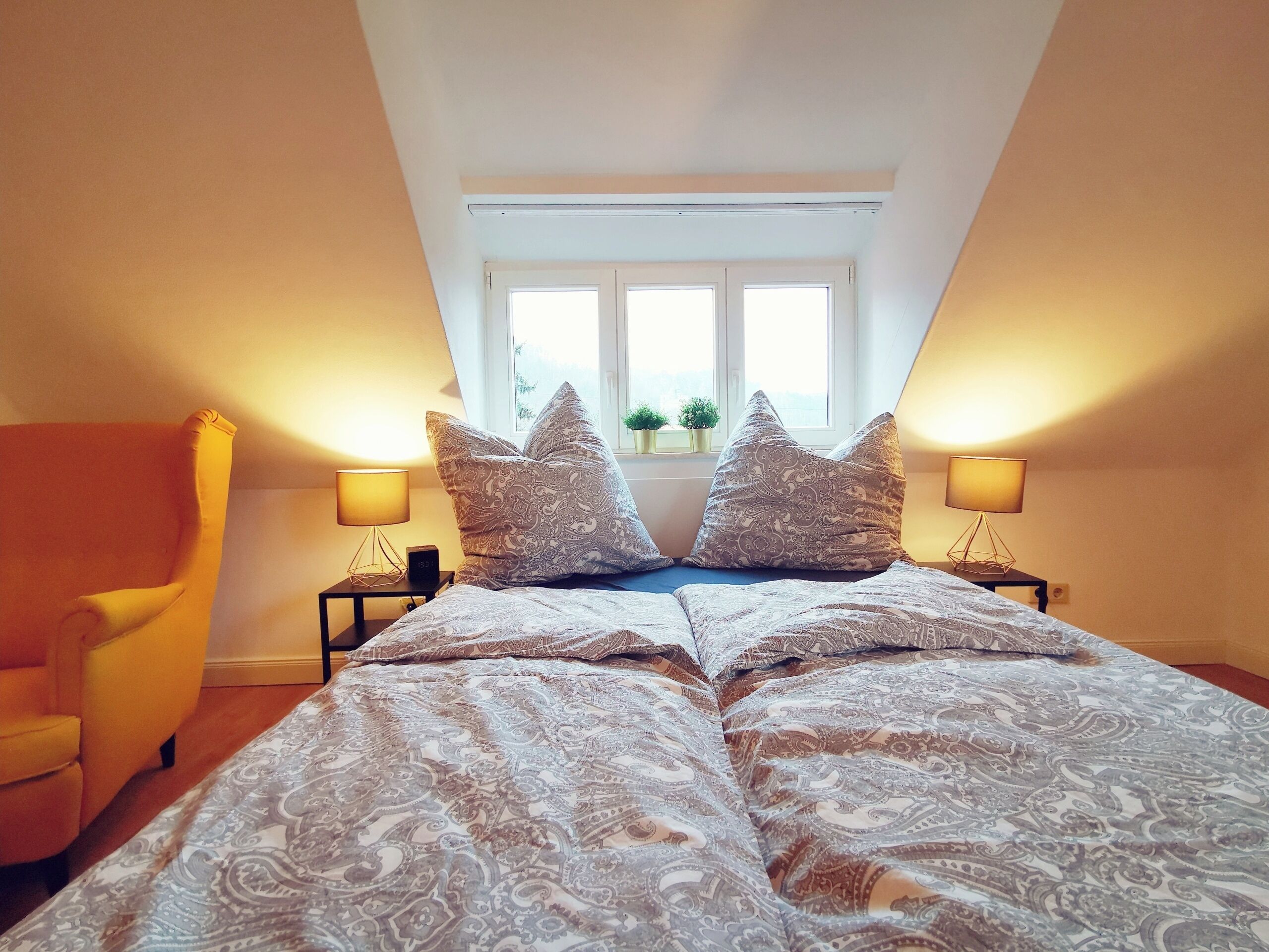 Un dormitorio con una cama, dos lámparas de noche, una ventana y una silla.