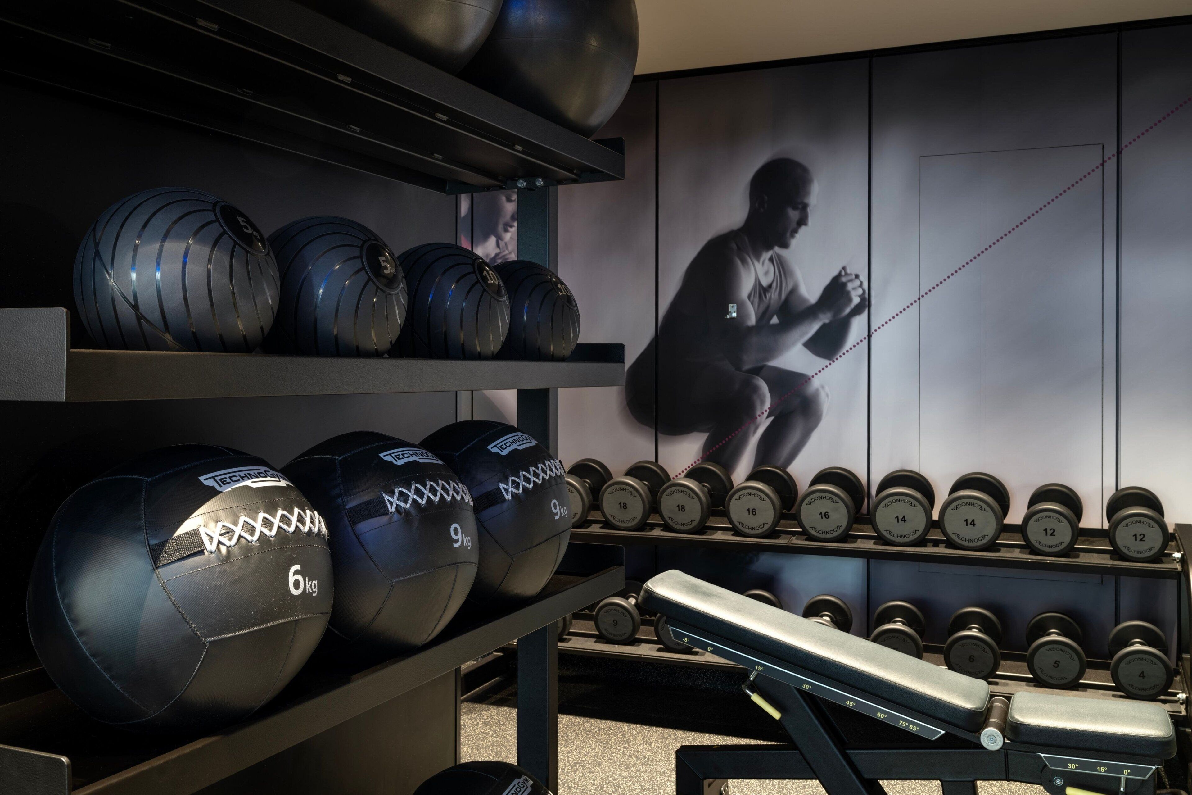 Un gimnasio con equipo de ejercicio, incluyendo balones medicinales y mancuernas, además de una banca.