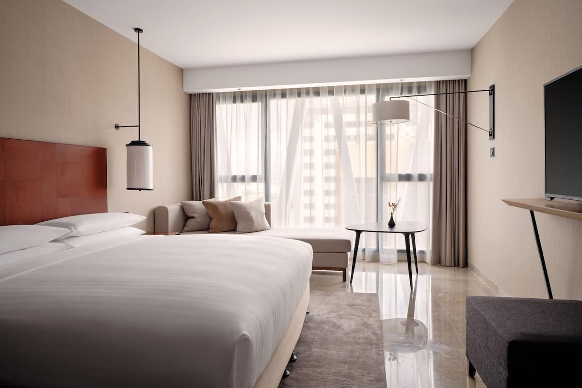A modern hotel room with a large bed, a small table, a chair, and a TV.
