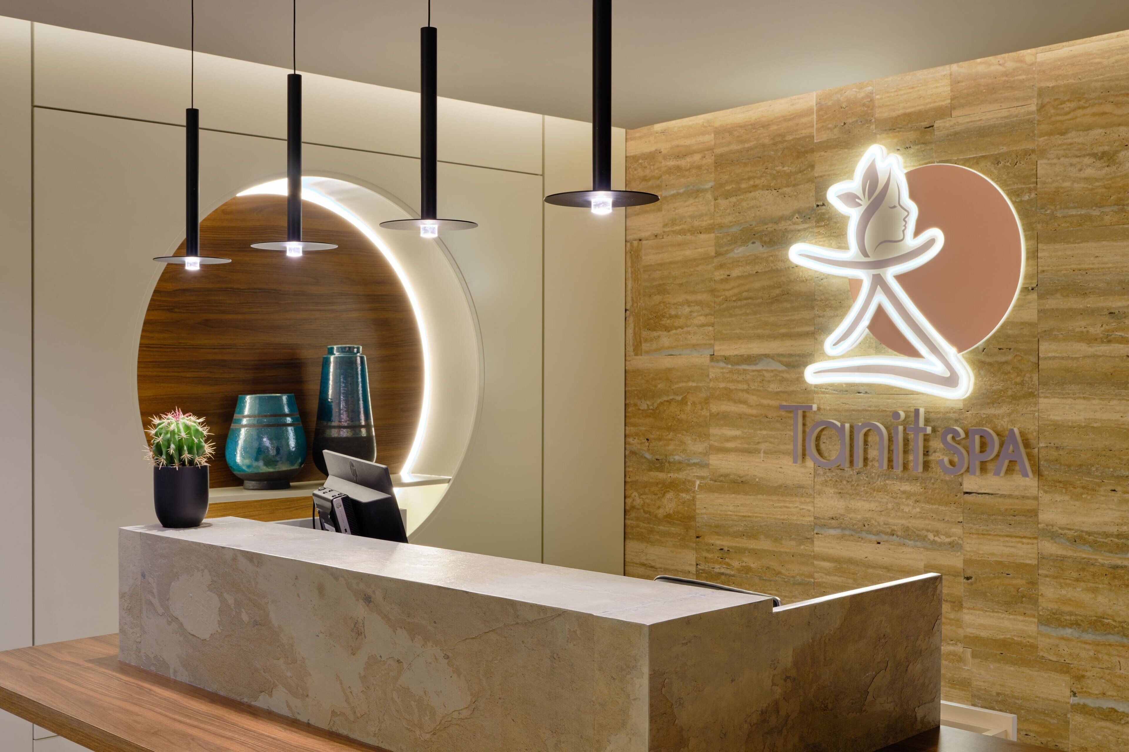 A reception desk with a wooden wall and a neon sign for Tanit SPA.